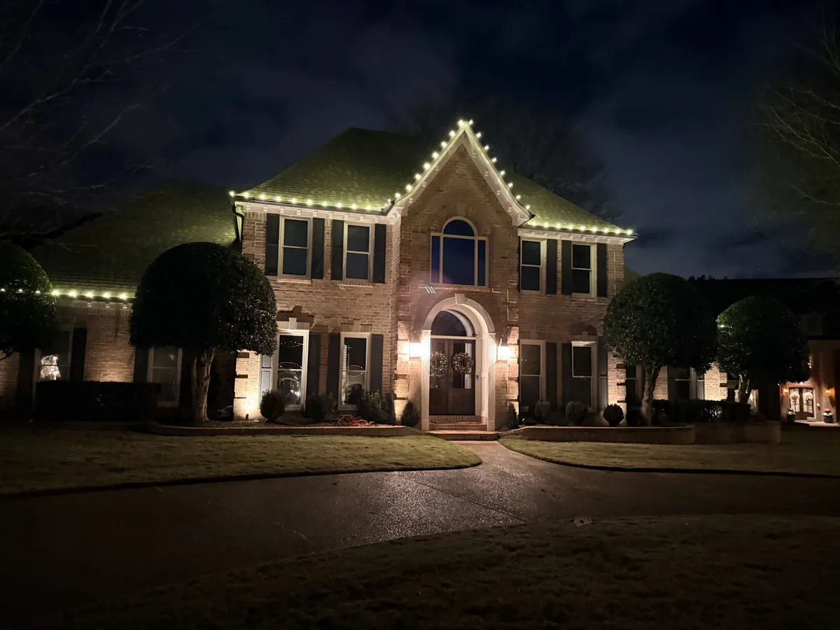 Two-story brick home with warm white lights along the roofline and front gable